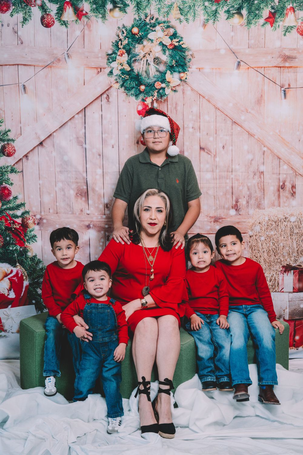 Family holiday photo session with coordinated red and green outfits against rustic barn door backdrop.