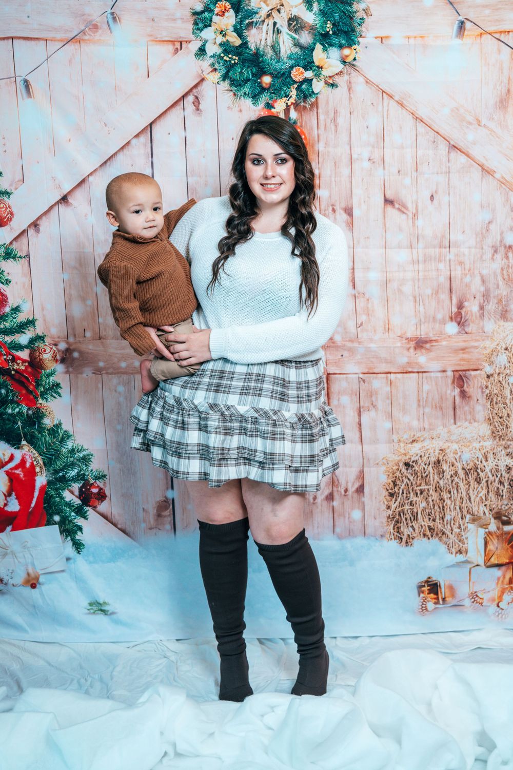 Winter photo session with plaid skirt and cozy sweaters against snowy backdrop and wooden wall.