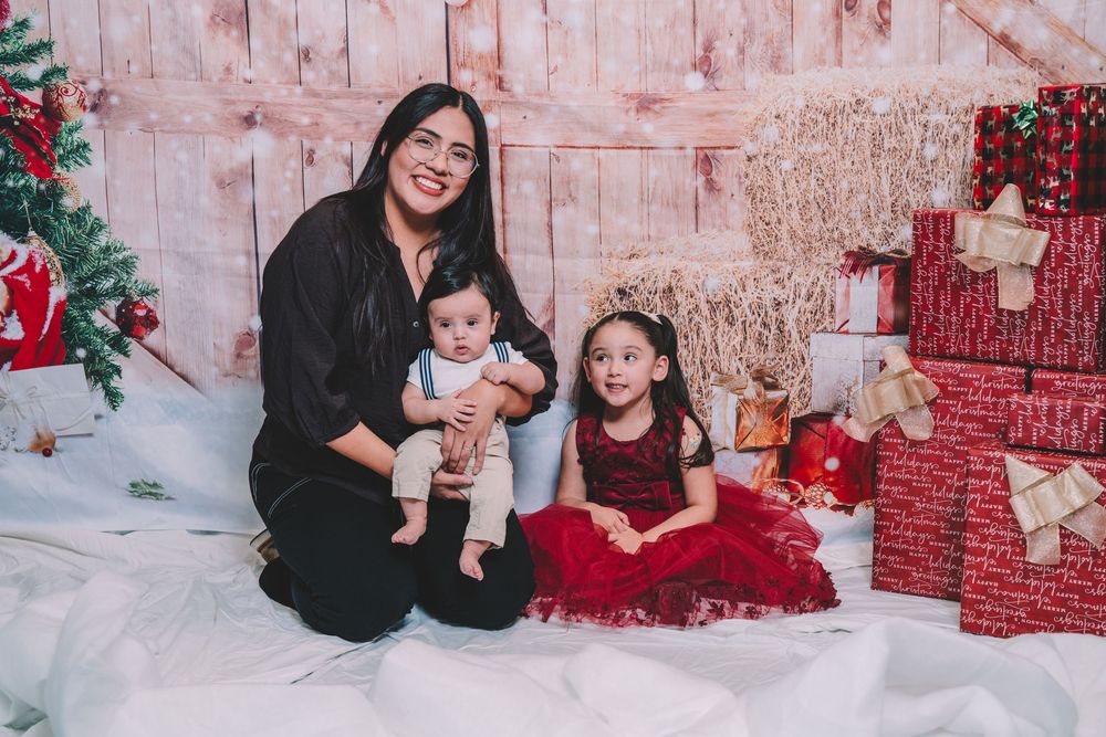 Holiday photo shoot with festive red decorations and wrapped presents against rustic backdrop.