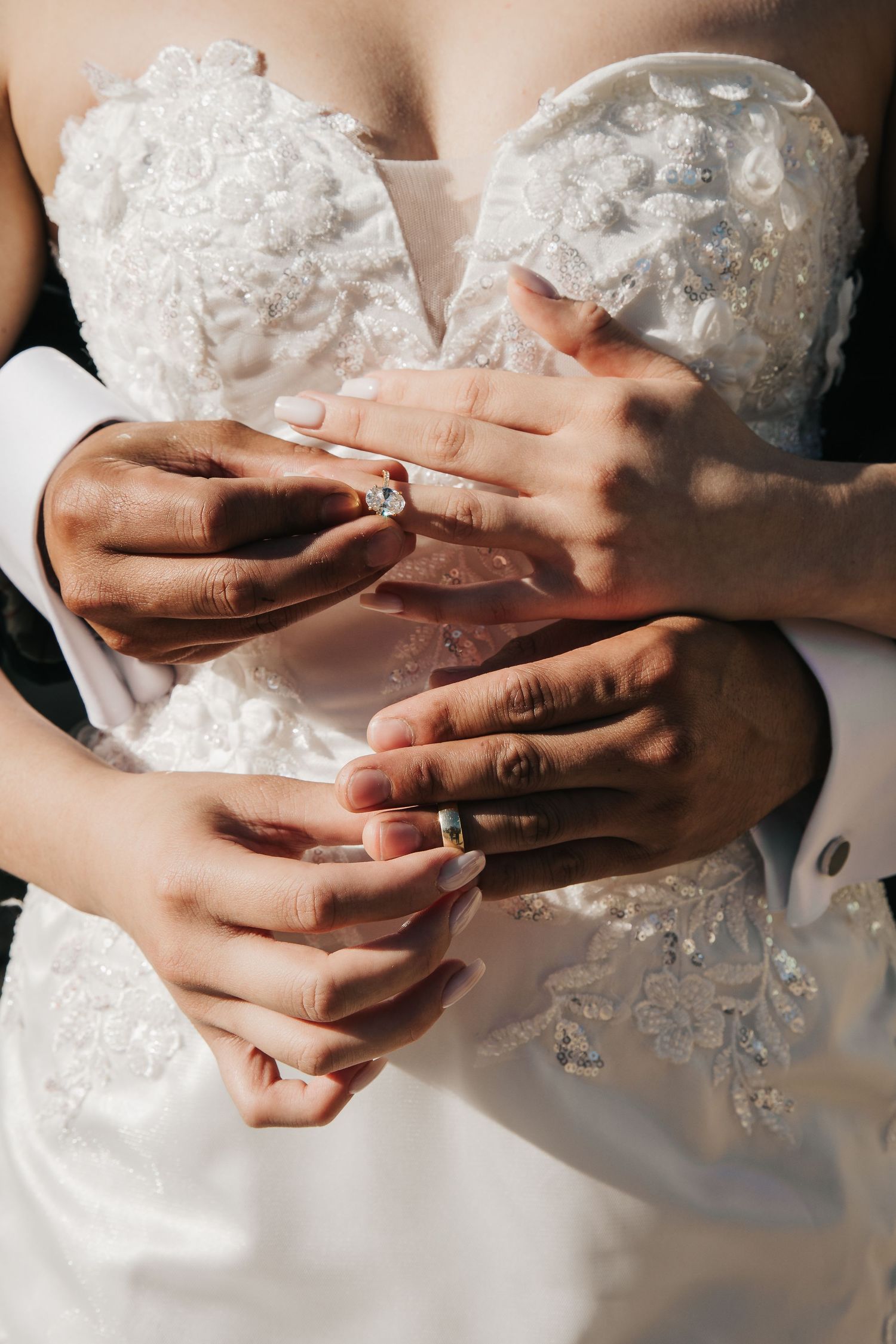 Close-up of hands holding delicate lace details on a white wedding dress in soft lighting.