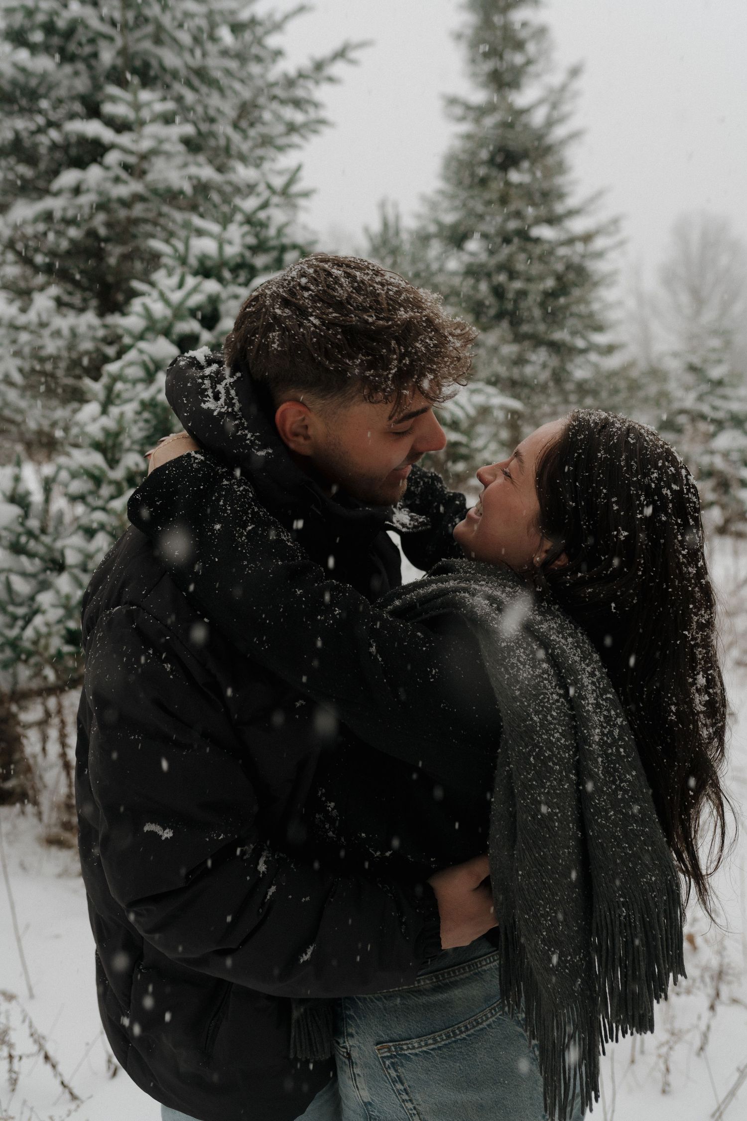 A romantic couple shares intimate moments in a snowy winter forest setting with evergreen trees in the background.
