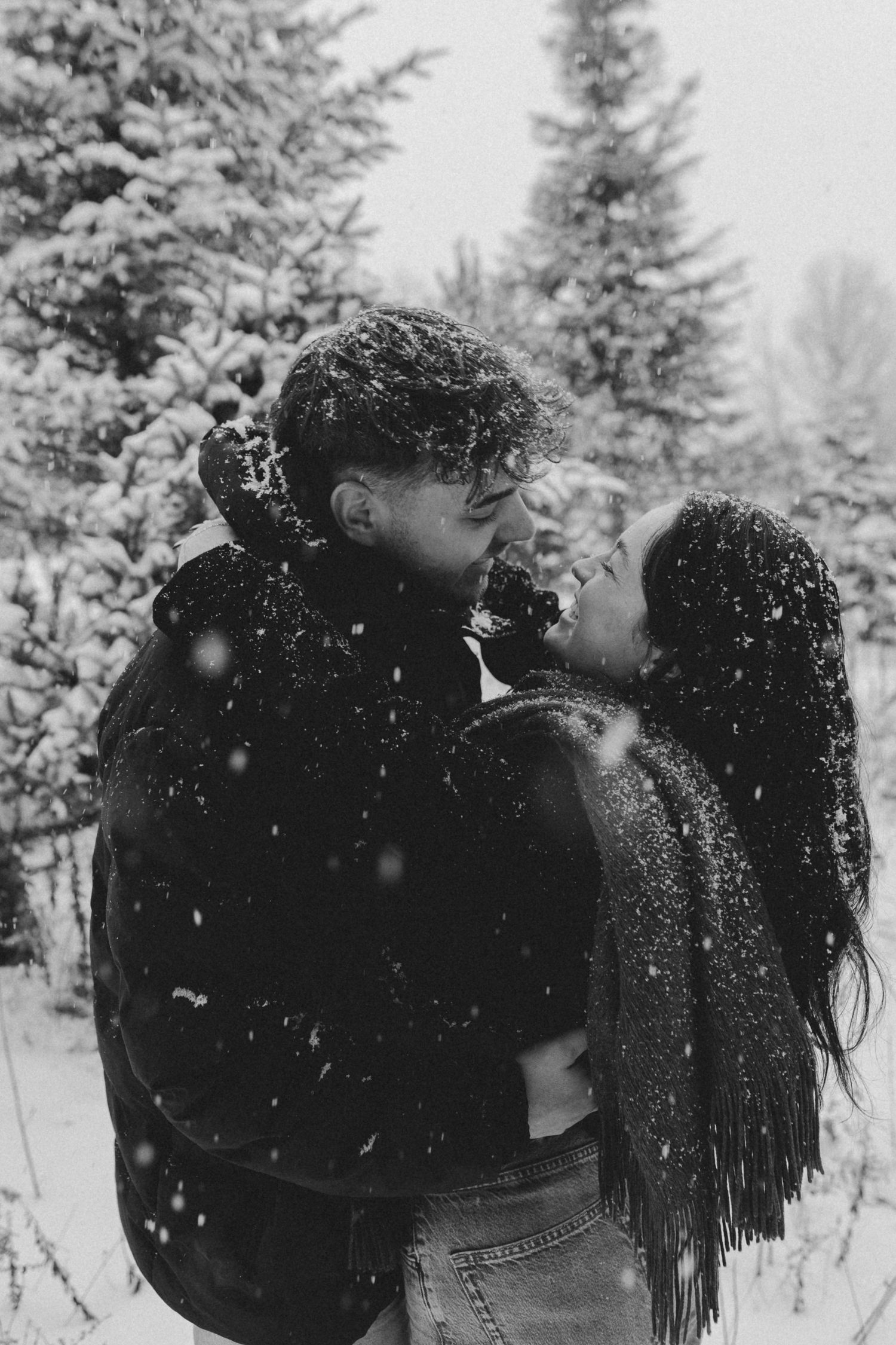 A romantic winter photoshoot among snow-covered evergreen trees in a serene forest setting.