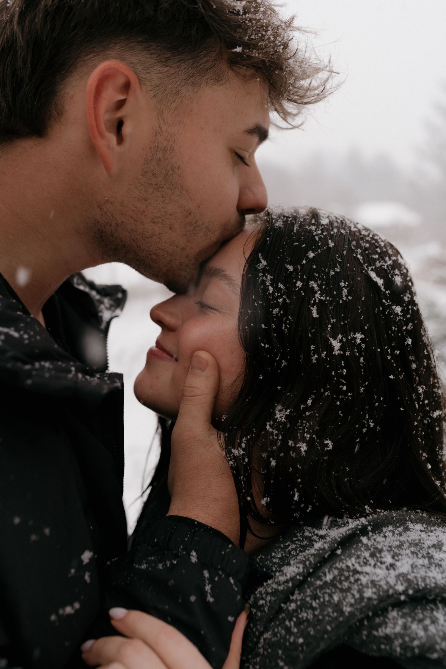 Intimate winter moment between couple sharing a tender kiss as snowflakes fall around them.