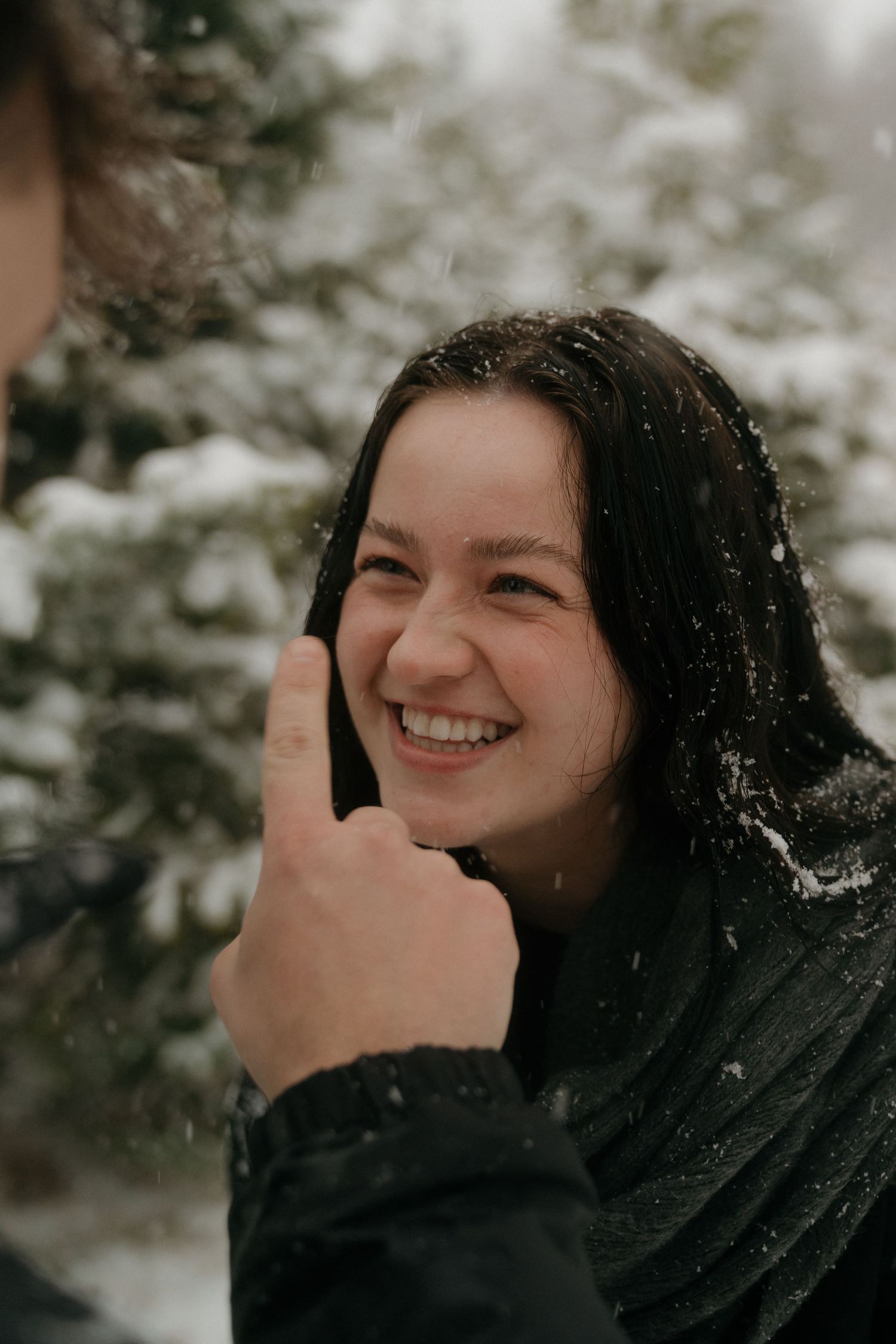 A person smiles joyfully while snowflakes fall in a winter forest setting.