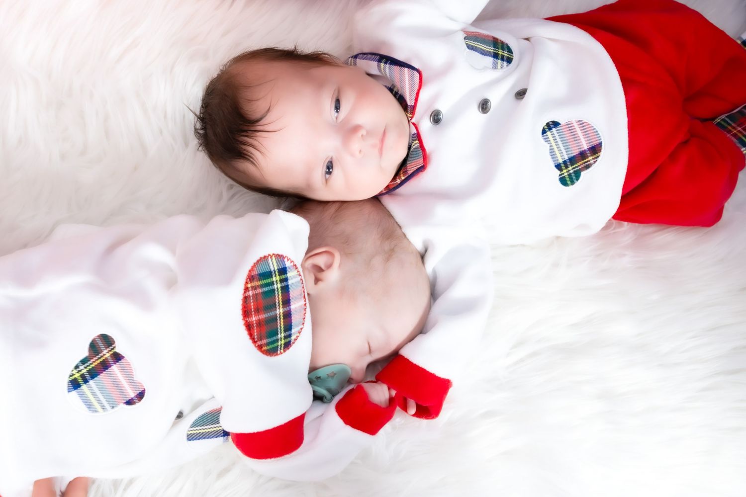 Baby in red and white Christmas outfit lying on soft white blanket with plaid accents.