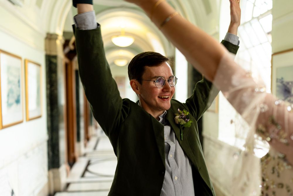 Person celebrating joyfully with raised arms in a hallway with artwork on the walls.