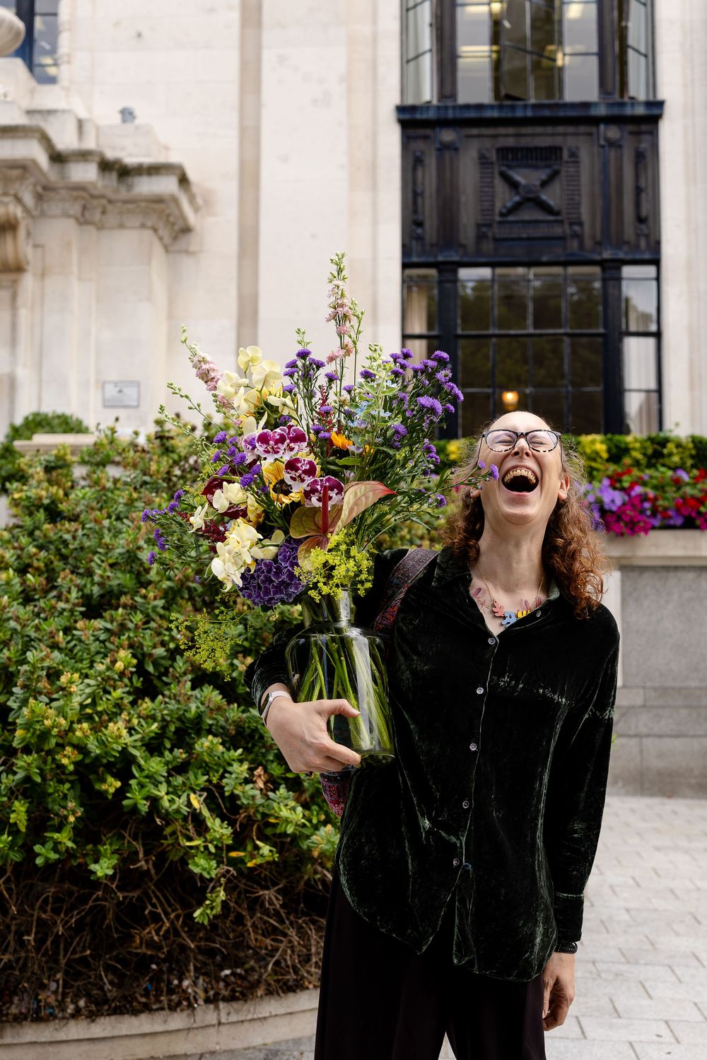 Joyful moment captured outdoors against a classic stone building facade with flowering garden beds.