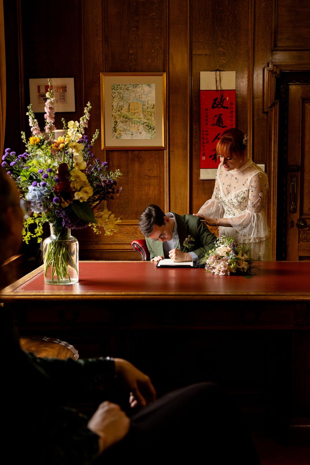 Elegant floral arrangements with purple and white flowers displayed on dark wooden shelves with framed artwork.