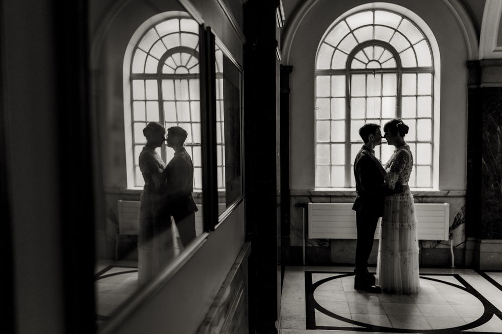 A romantic silhouette of a couple standing in front of an arched window with their reflection visible in a mirror.