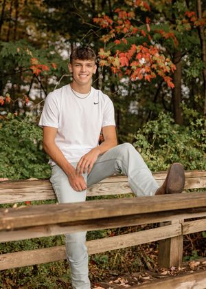 Someone sitting on a wooden bench surrounded by autumn foliage and trees.