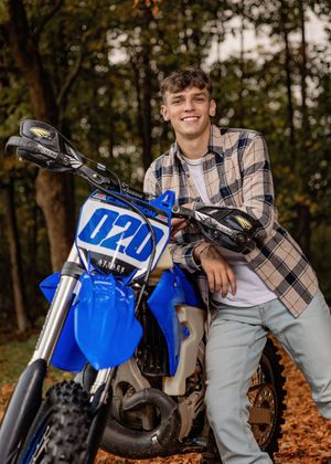 A blue dirt bike motorcycle positioned in autumn foliage with fallen leaves on the ground.