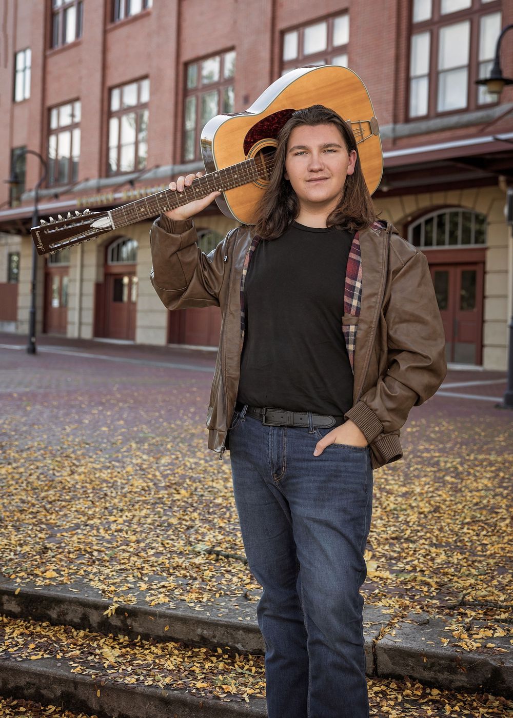 Fall portrait session with guitar against brick building surrounded by autumn leaves.