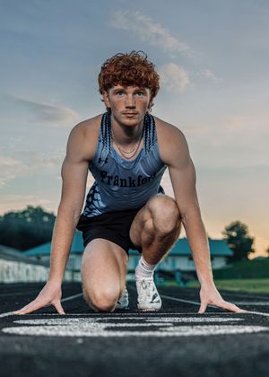 Track athlete in starting position on running track at dusk.