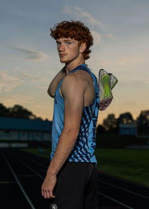 Track athlete in blue tank top training at sunset on outdoor track.