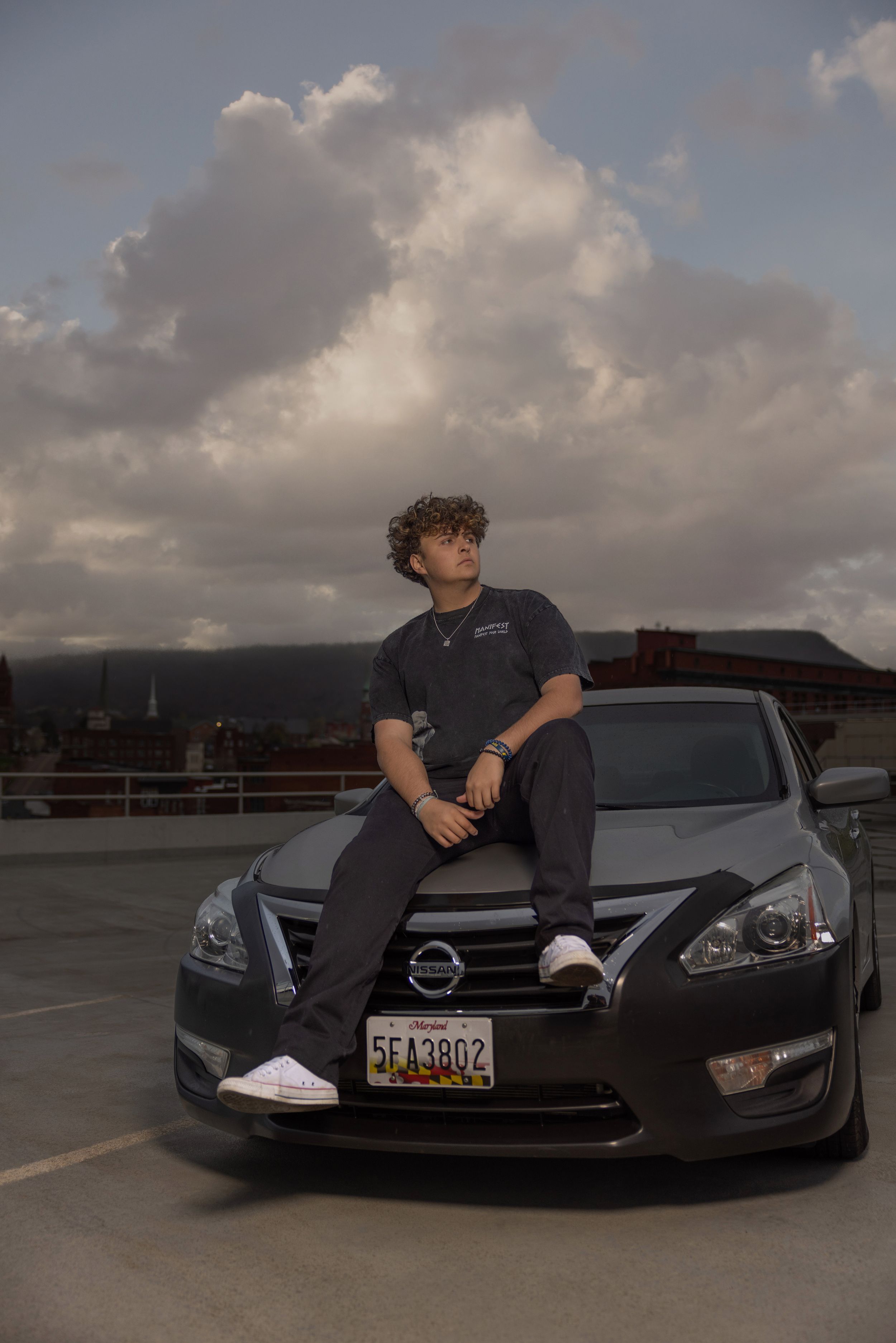 A dark colored Nissan vehicle parked in a lot during sunset with cloudy skies.