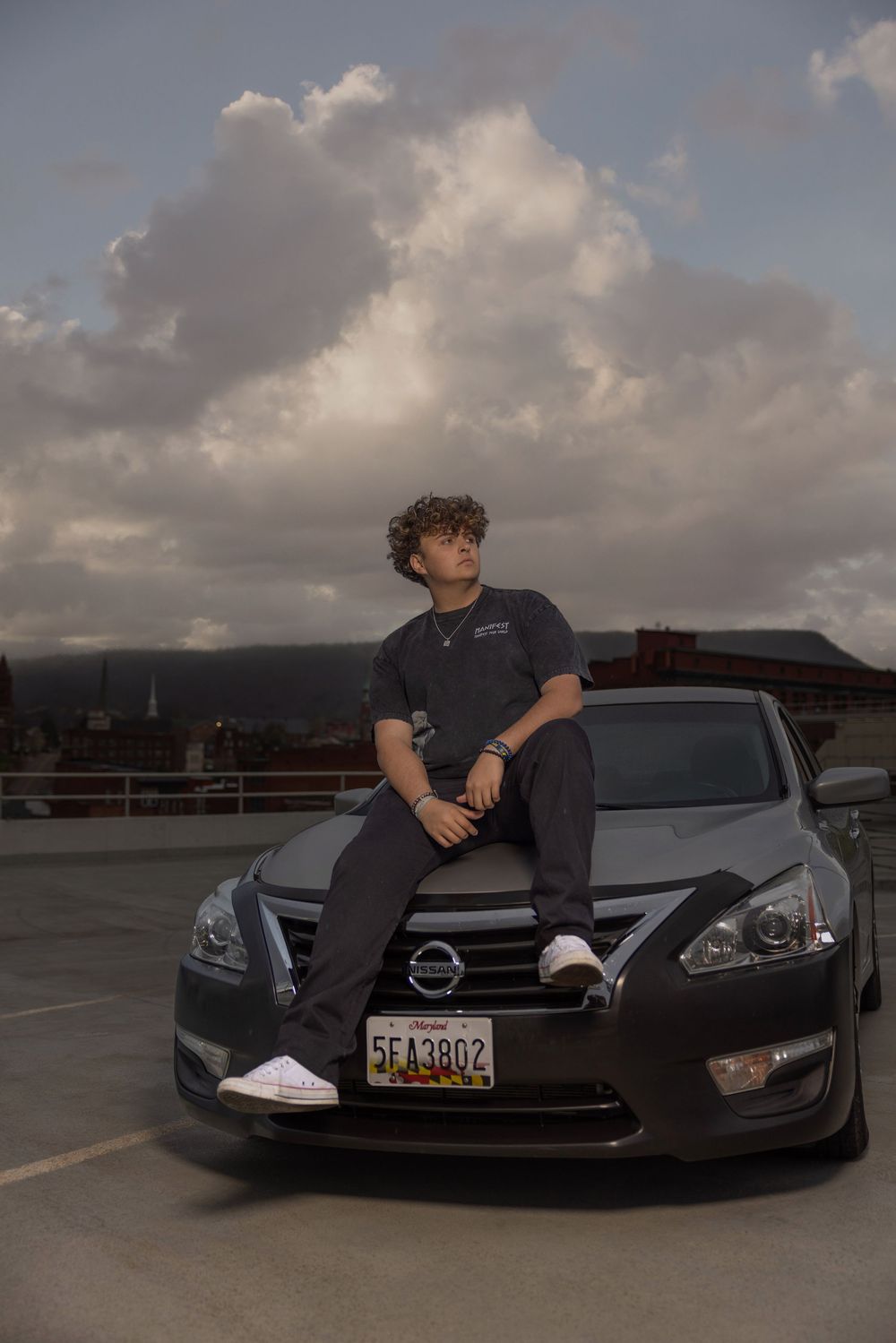 A dark colored Nissan vehicle parked in a lot during sunset with cloudy skies.