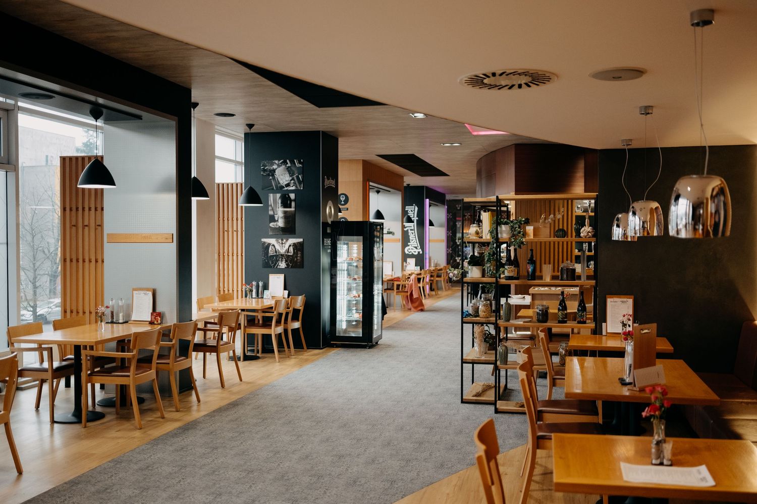 Modern restaurant interior with wooden furniture, pendant lights and dark accent walls.
