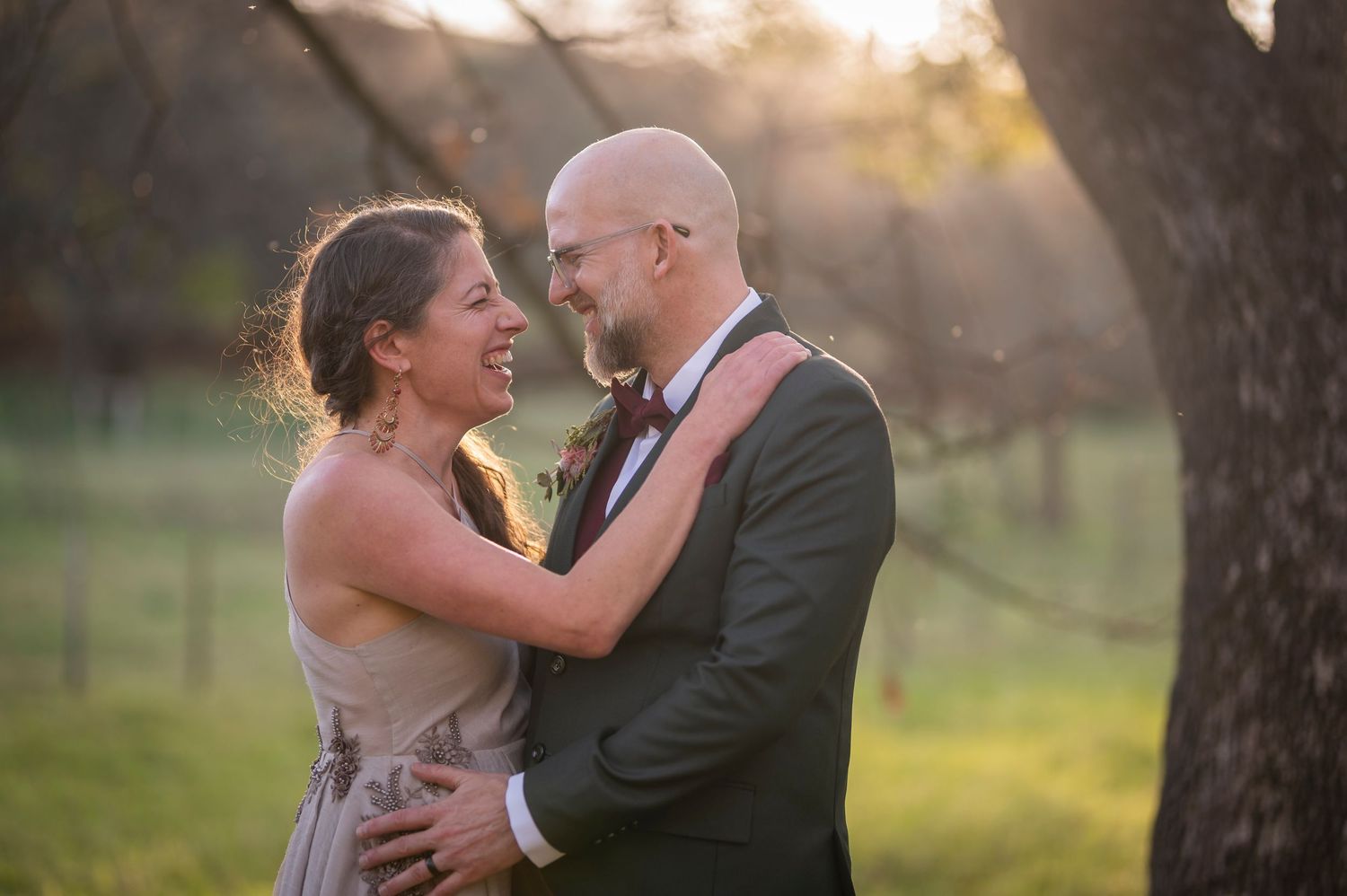 A romantic couple embraces during sunset in a dreamy outdoor setting with golden light filtering through trees.