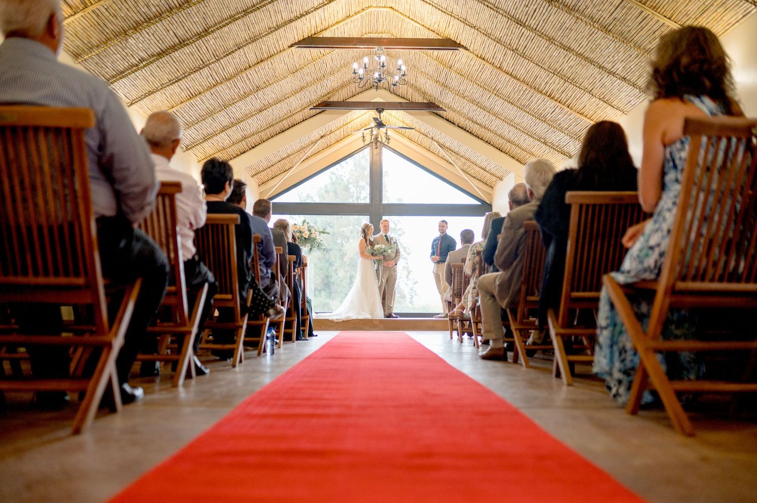 A panoramic view of a rustic wooden chapel interior with a red carpet aisle leading to a bright window at the altar.