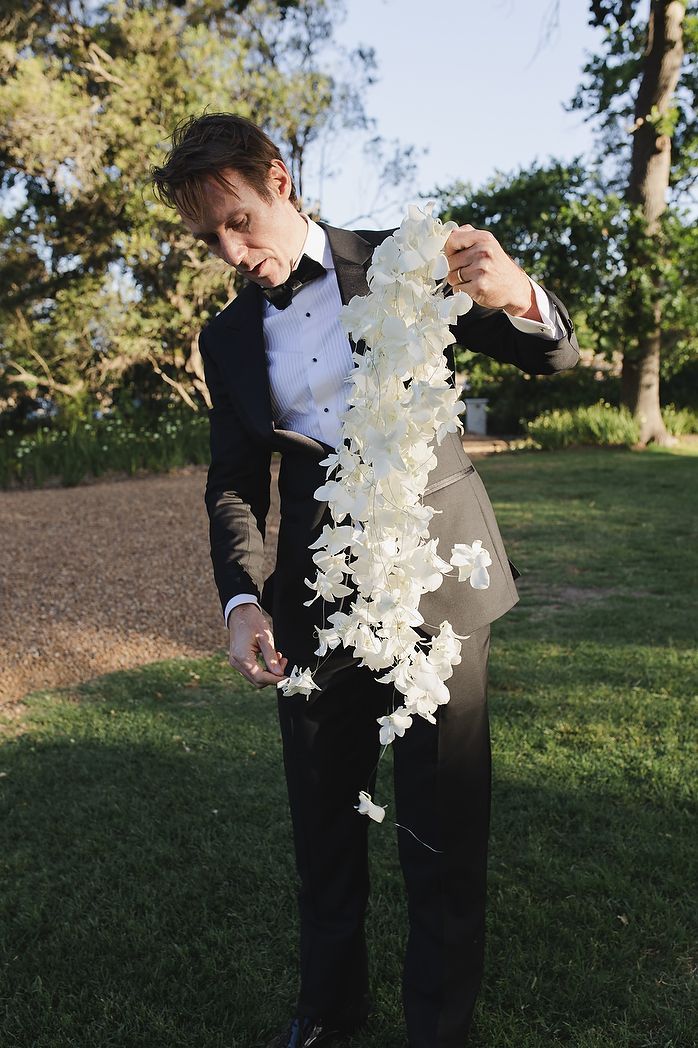 Groom holding orchid bouquet with textured white florals.