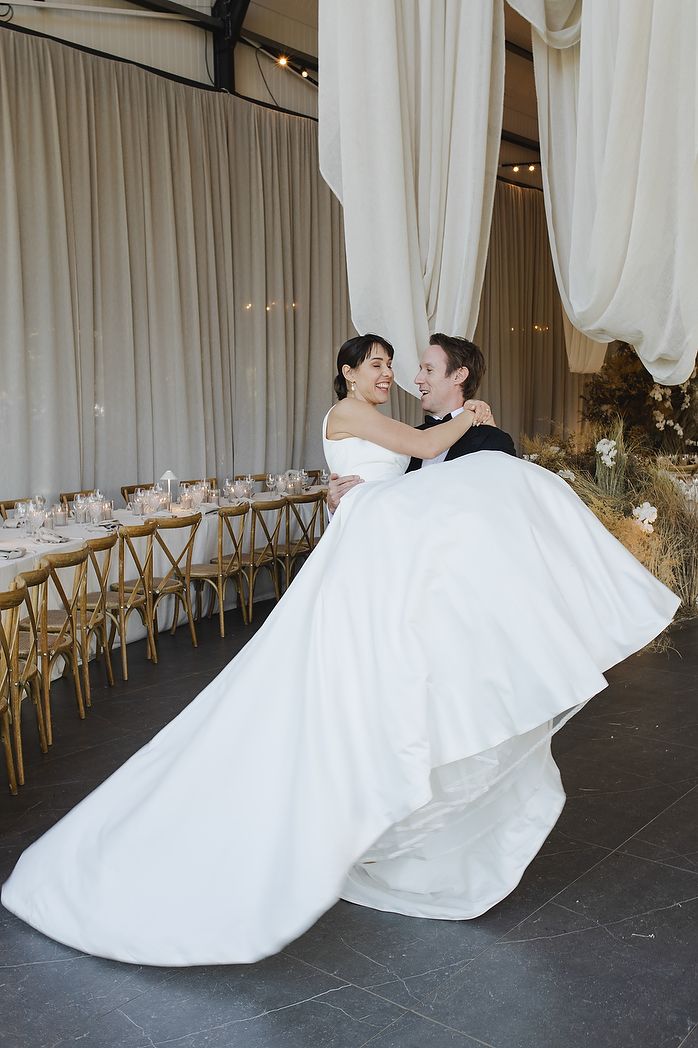 Groom lifting bride happily in reception area.