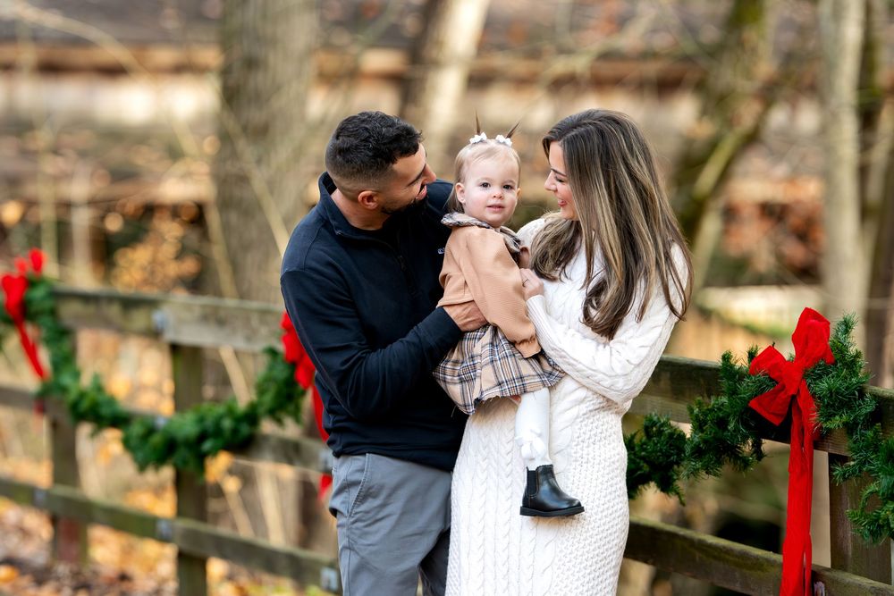 Family of three sharing a tender moment by a Christmas garland fence in an autumn woodland setting.