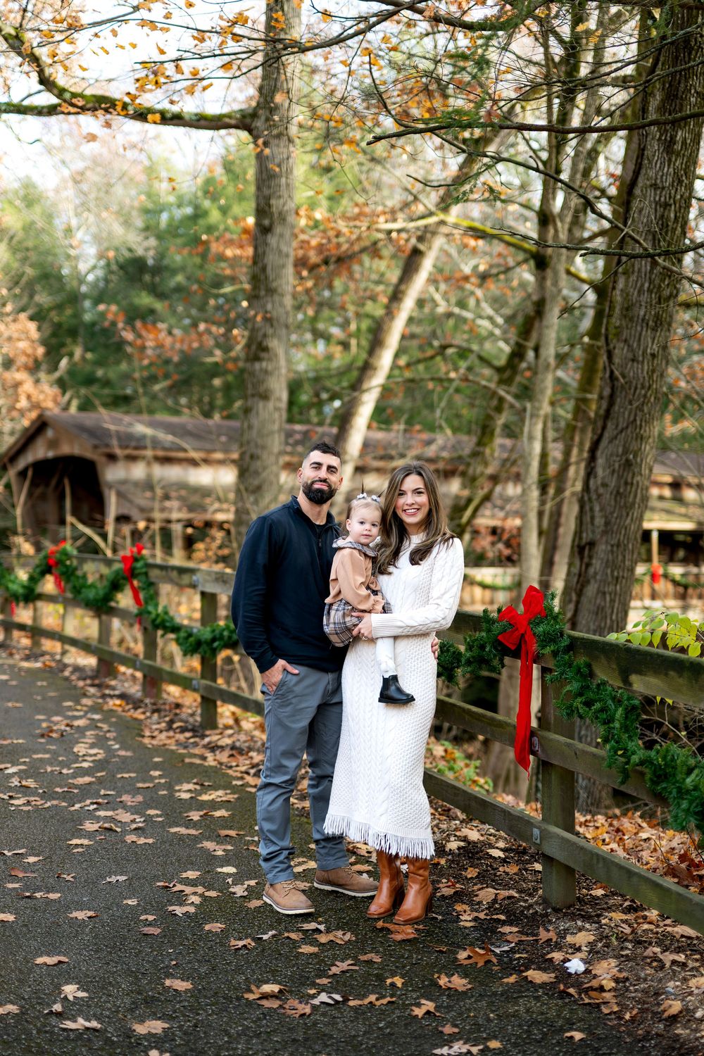 Young family posing with baby by festive garland fence in a scenic autumn forest path.