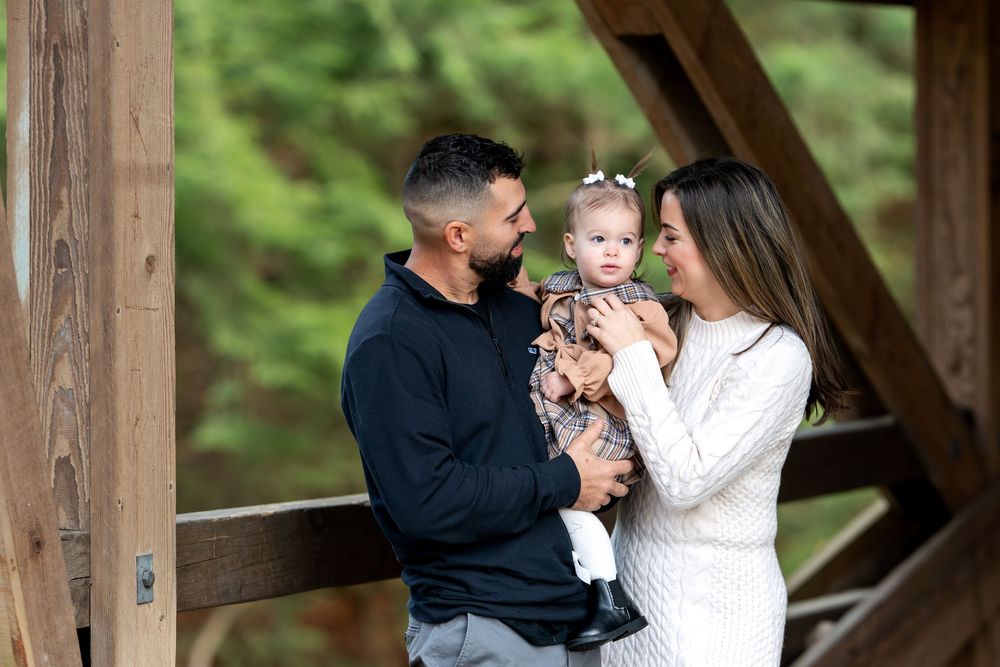 Couple sharing tender moment with baby daughter on rustic wooden bridge in autumn forest.