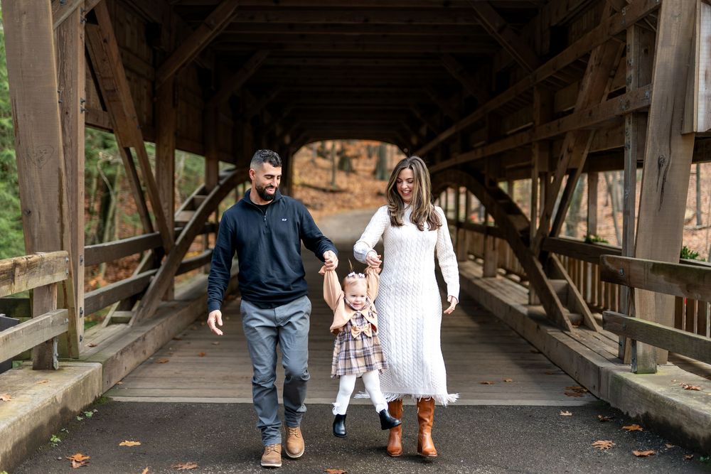 Young family walking hand-in-hand through charming covered wooden bridge in fall setting.