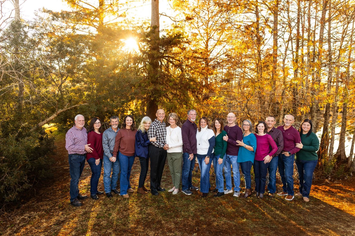 Large group of people silhouetted against golden sunset through autumn trees.