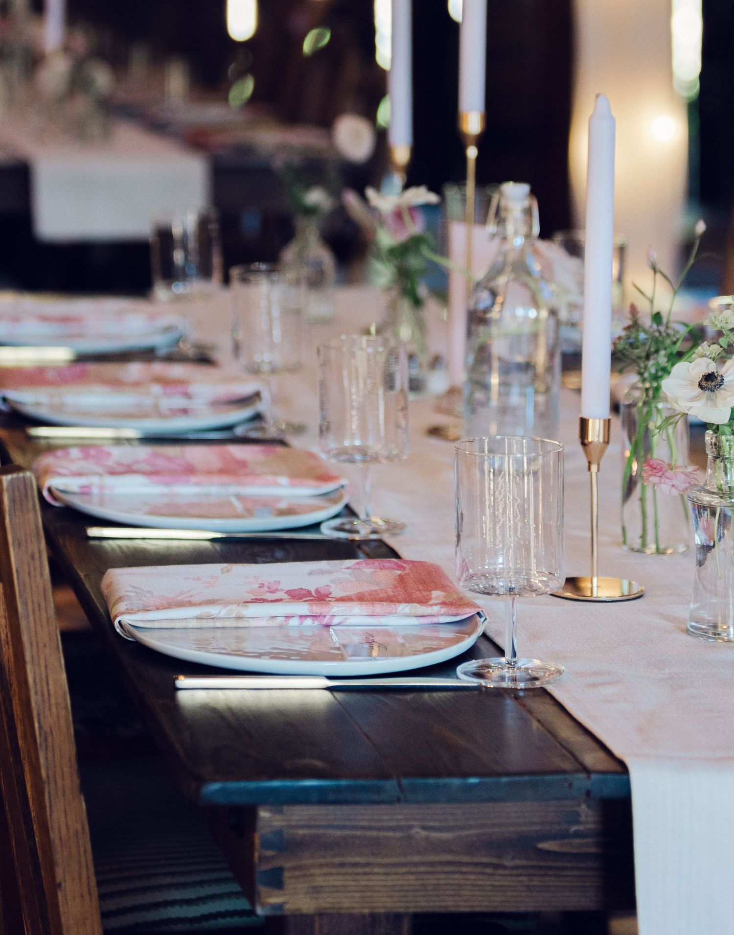 A long dining table set with elegant place settings, white plates, and glassware on a dark wooden surface.