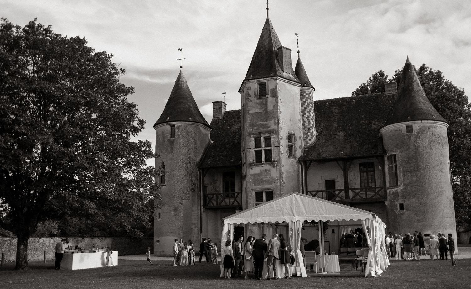 A wedding celebration setup with white tents and guests gathered on the grounds of a historic French chateau.