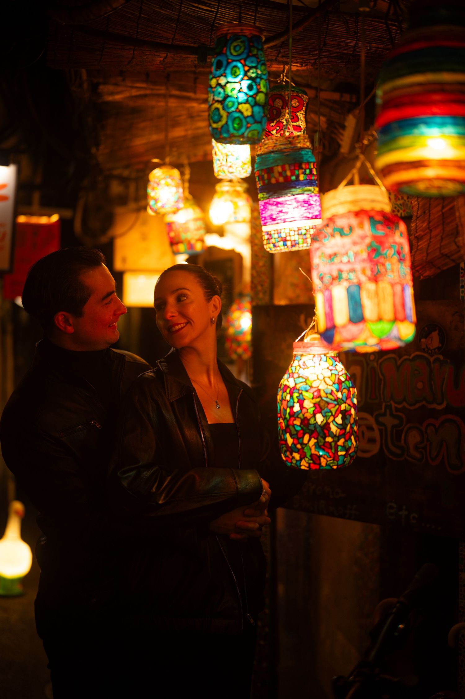 Couple smiling together surrounded by vibrant colorful mosaic lanterns in a dimly lit shop.