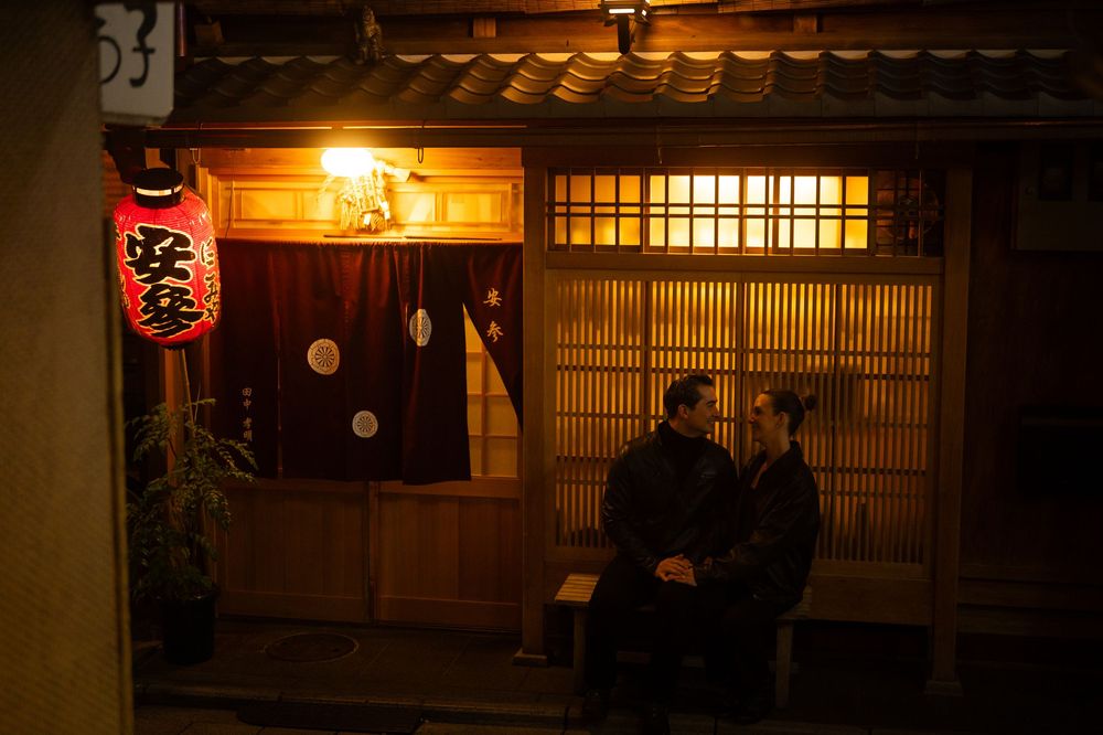 Couple standing together outside a warmly lit traditional Japanese restaurant at night.
