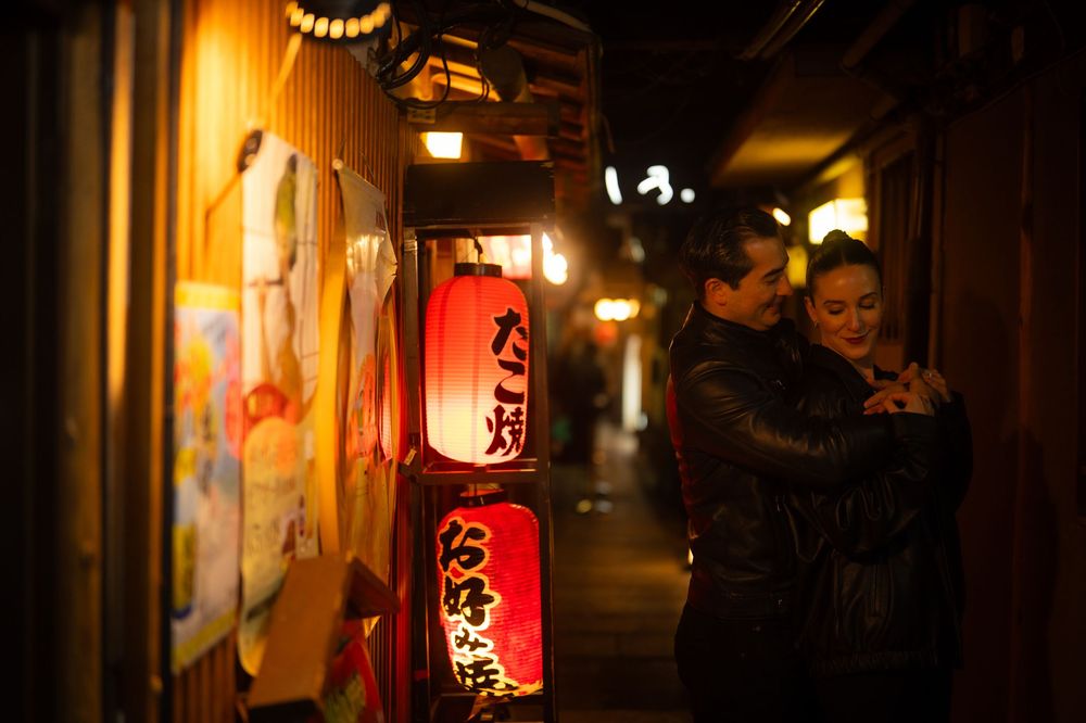 Couple embracing in a vibrant Japanese alley lined with colorful red lanterns at night.