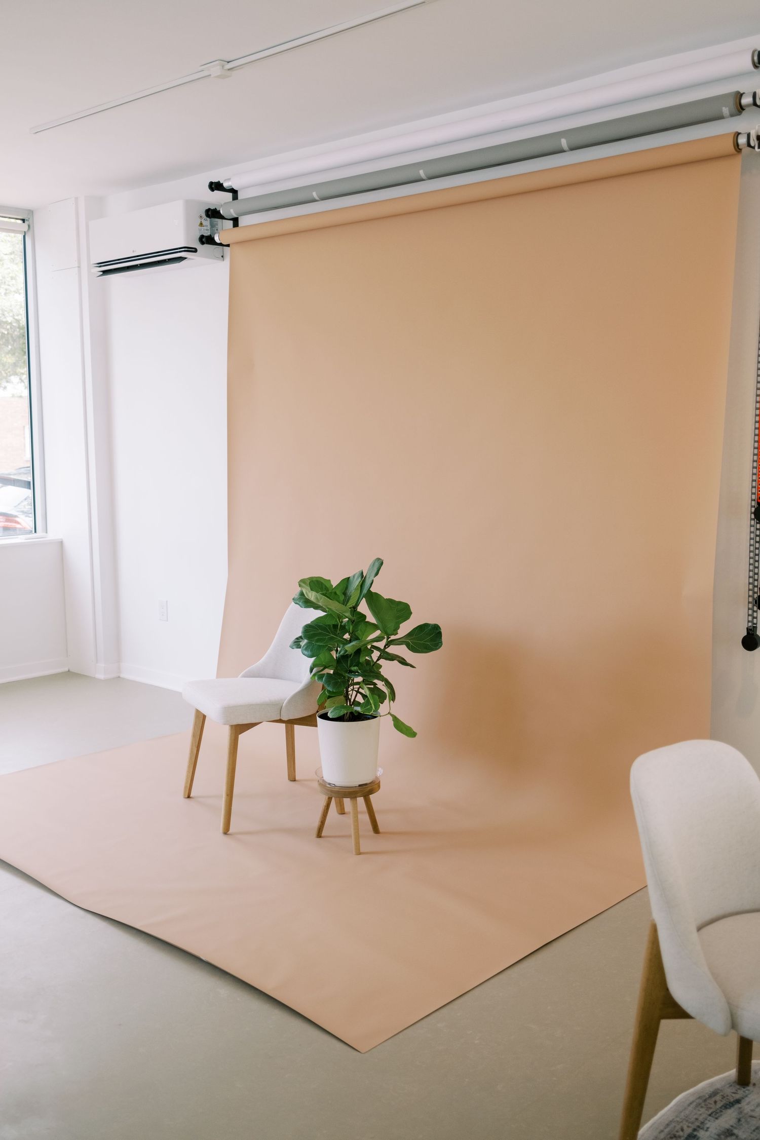 Modern white lounge chair with wooden legs shown from different angles next to a potted green plant against beige background.