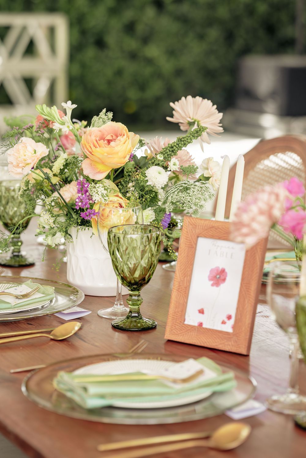 Elegant table settings with soft peach and green floral centerpieces, place cards, and delicate glassware for a garden party.