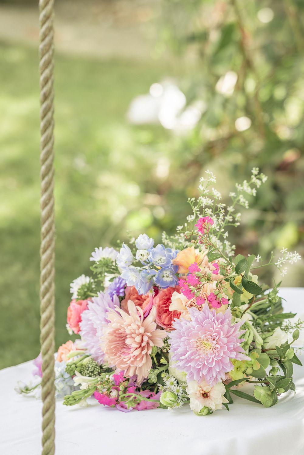 Beautiful pink and purple floral arrangement with dahlias and greenery on a white swing in a garden setting.