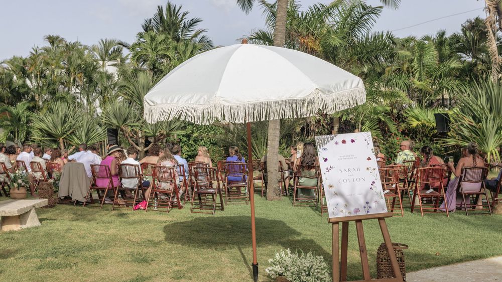 Panoramic view of a tropical outdoor wedding venue with palm trees and white parasols.