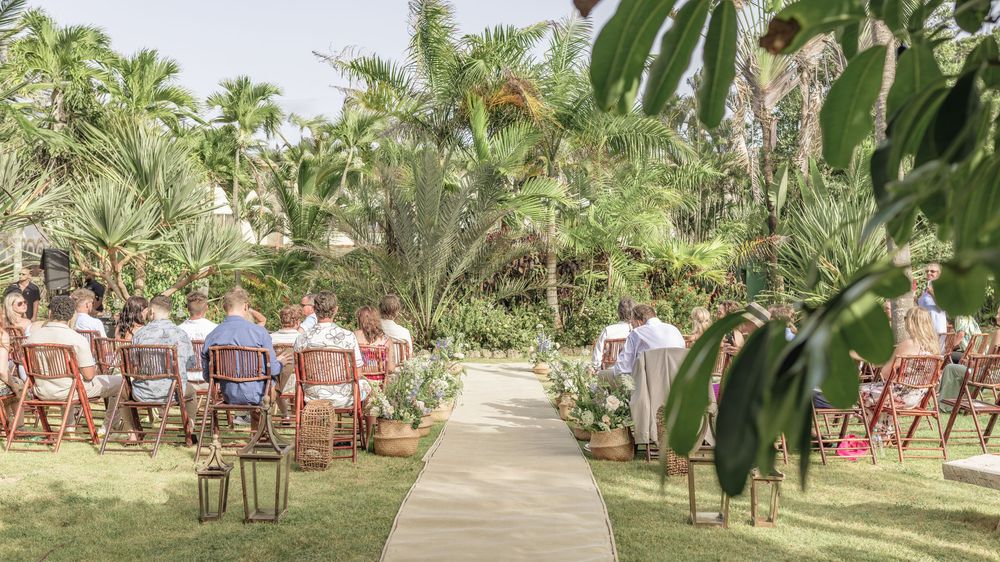 Palm tree lined pathway with white chairs set up for an outdoor tropical wedding ceremony.
