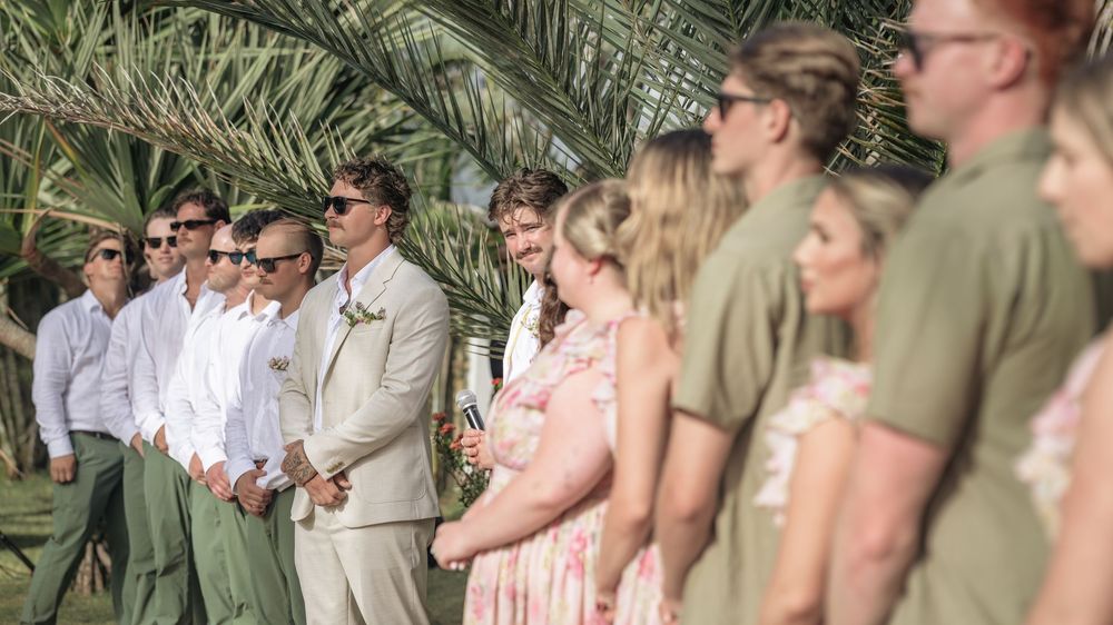 Wedding guests gathered outdoors under palm trees during a ceremony.