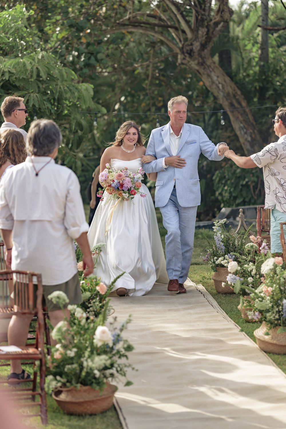 Wedding guests in white attire gathering along a garden pathway during an outdoor celebration.