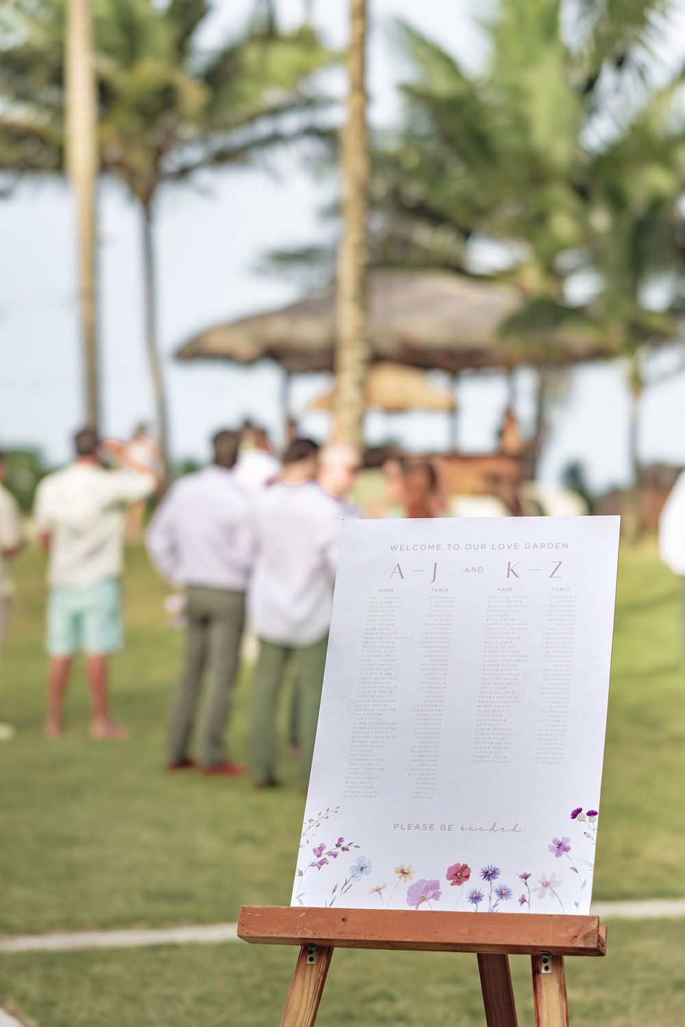Blank white signs displayed on wooden easels at an outdoor tropical wedding venue with palm trees.