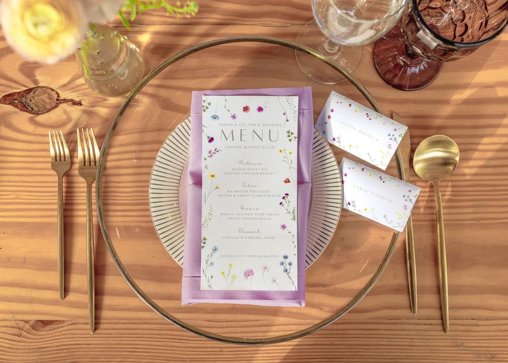 Elegant table settings with menus and gold cutlery on rustic wooden surfaces at an outdoor event.