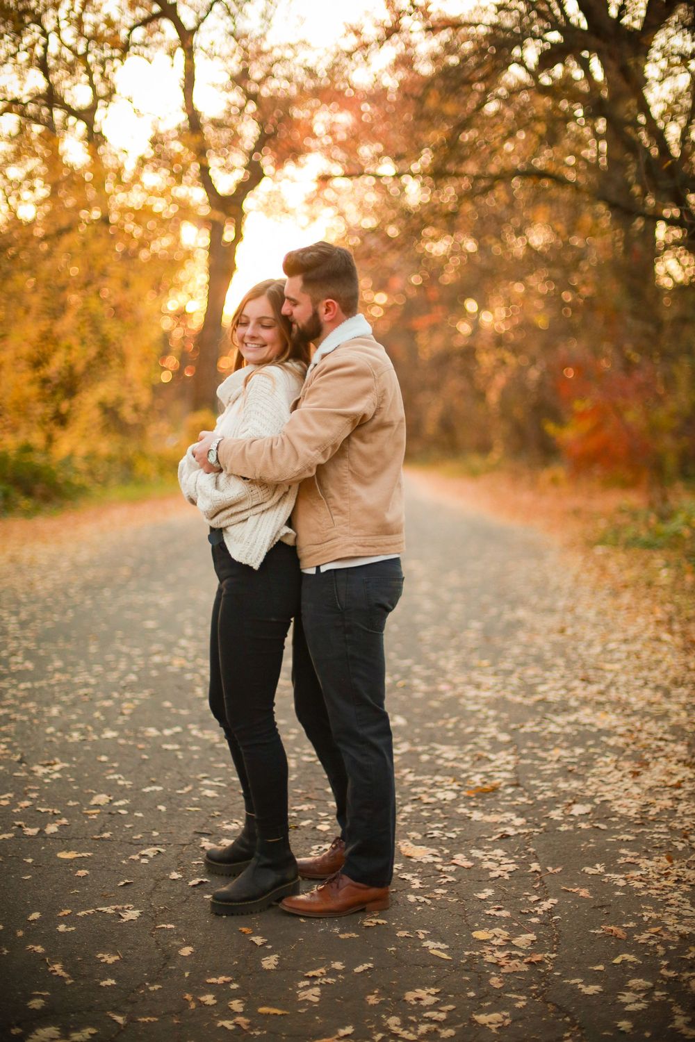 Couple sharing romantic moments on a leaf-covered autumn path at sunset.