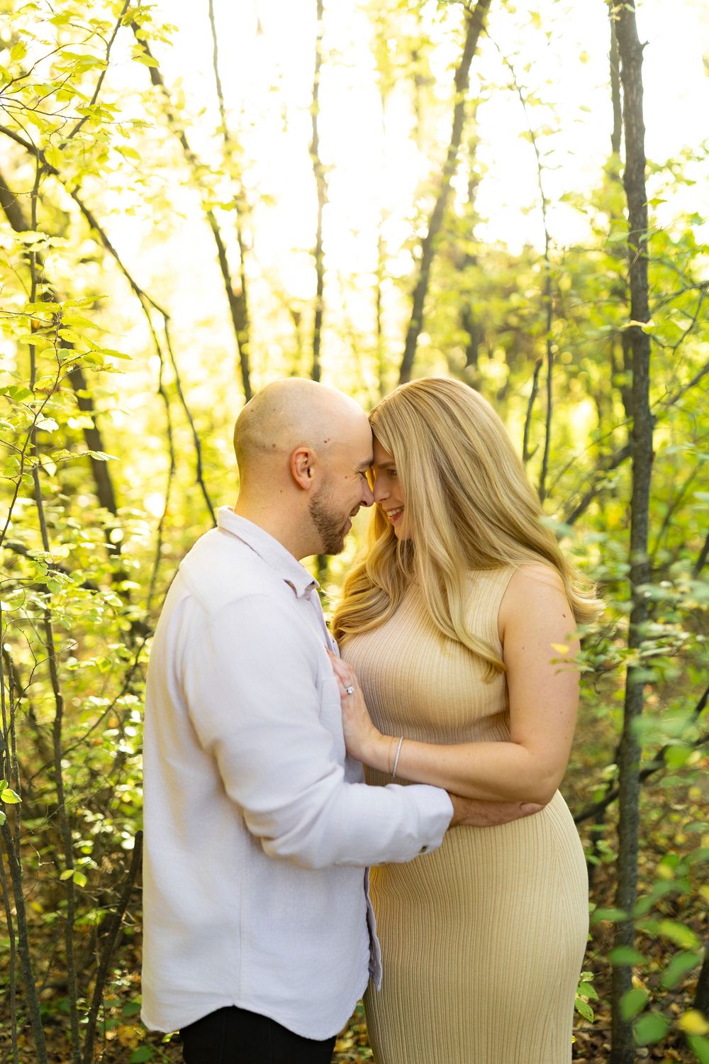 A couple embraces tenderly in a forest bathed in warm golden light.