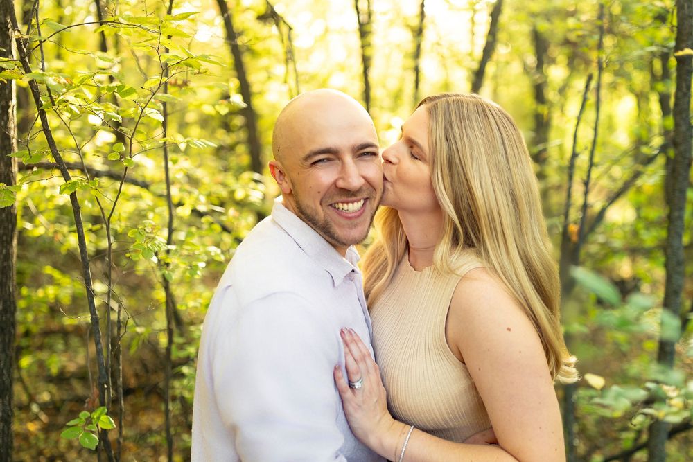 A couple shares an intimate moment in a sunlit forest with golden leaves.
