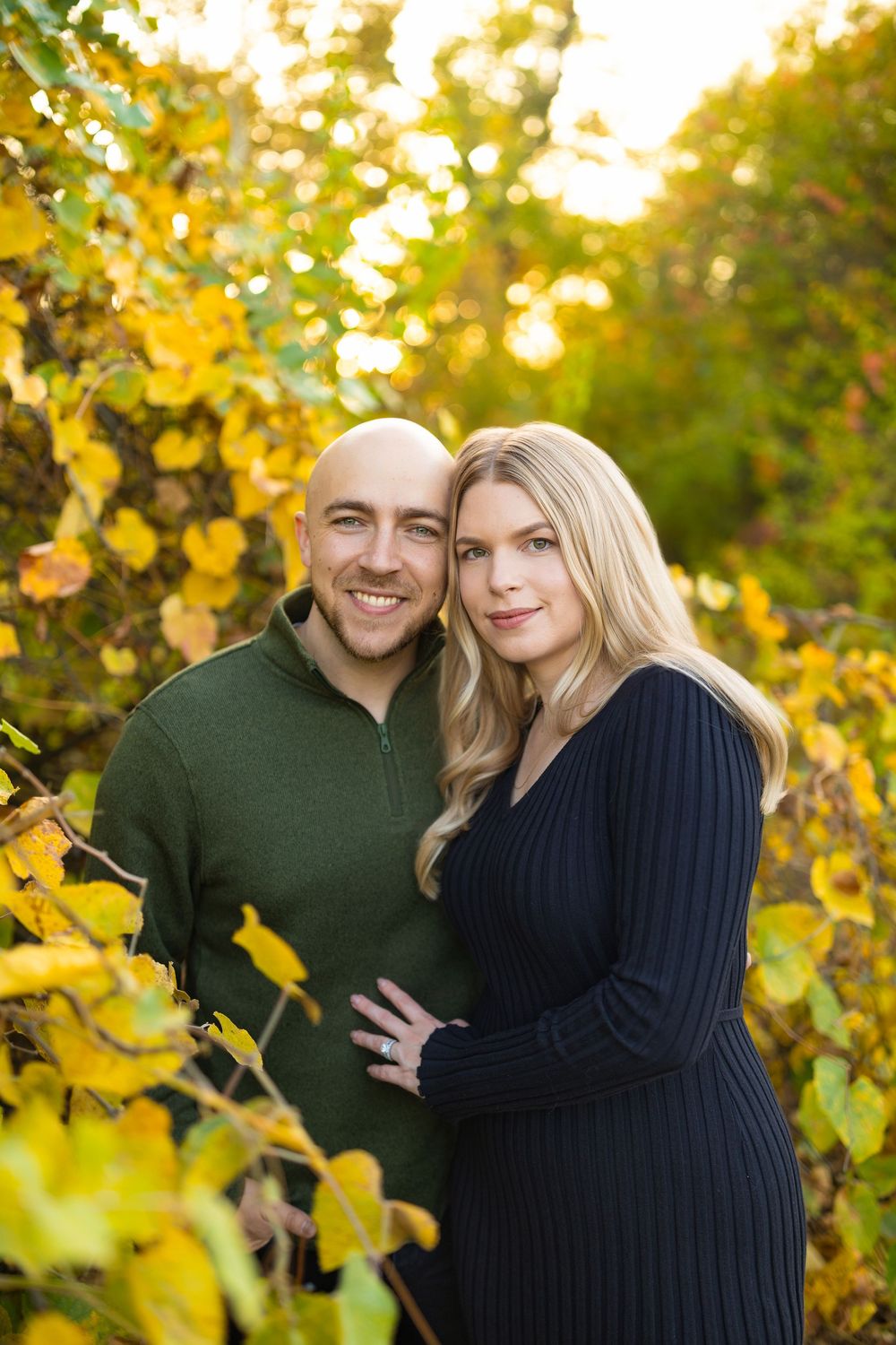 Couple in dark sweaters sharing affectionate moments among autumn foliage.