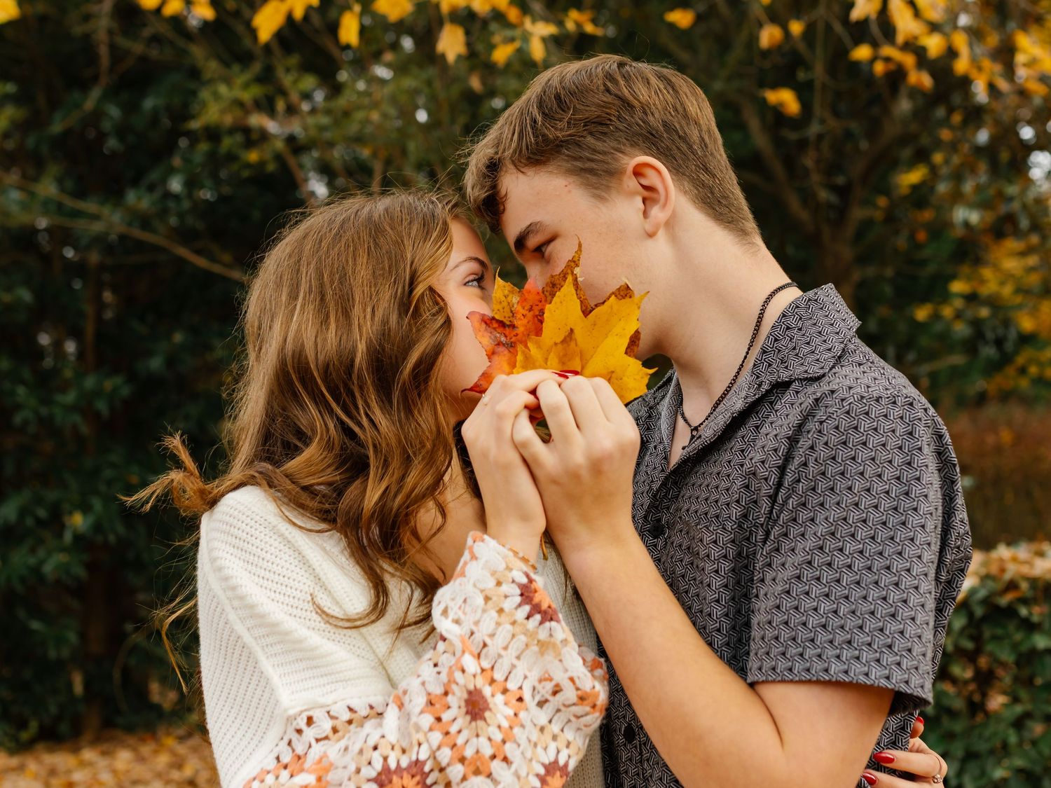 A romantic autumn moment as a couple shares a yellow leaf against a backdrop of fall foliage.