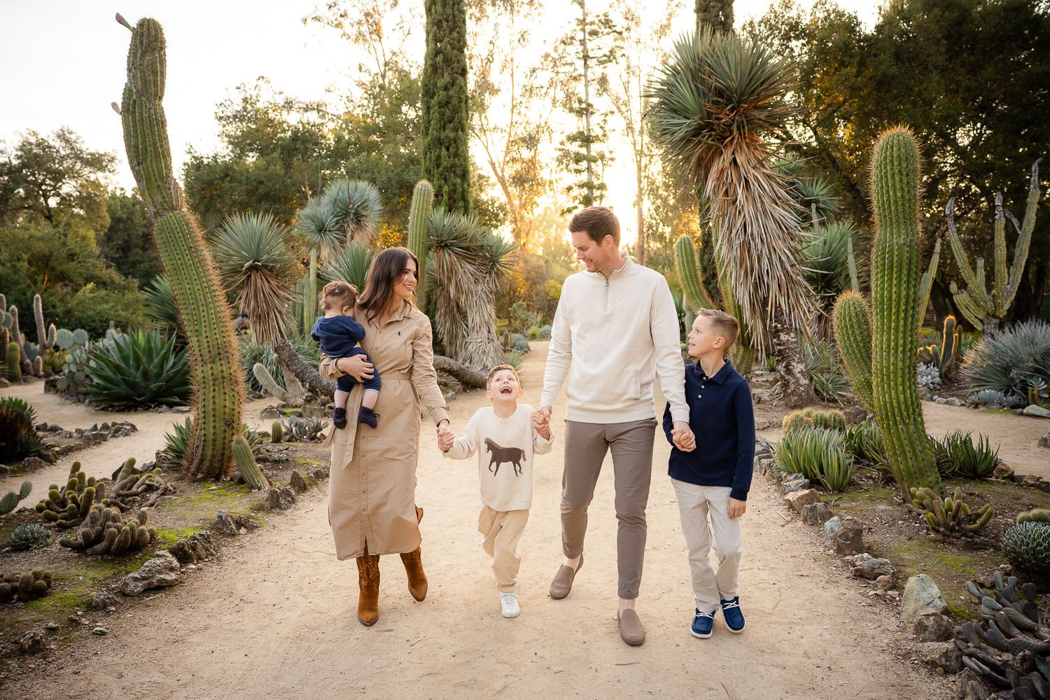 A family walks together through a desert botanical garden path lined with tall cacti at sunset in Palo Alto